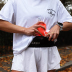 Person wearing a white t-shirt and shorts with a red EXEO water bottle and black waist bag.