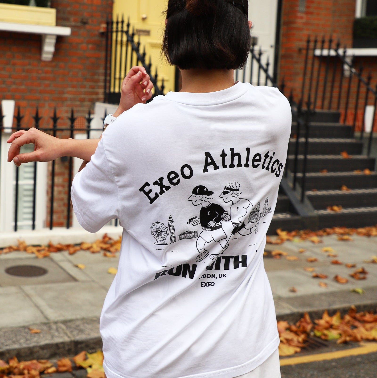 Person wearing a white 'Exeo Athletics' t-shirt with graphics outdoors.